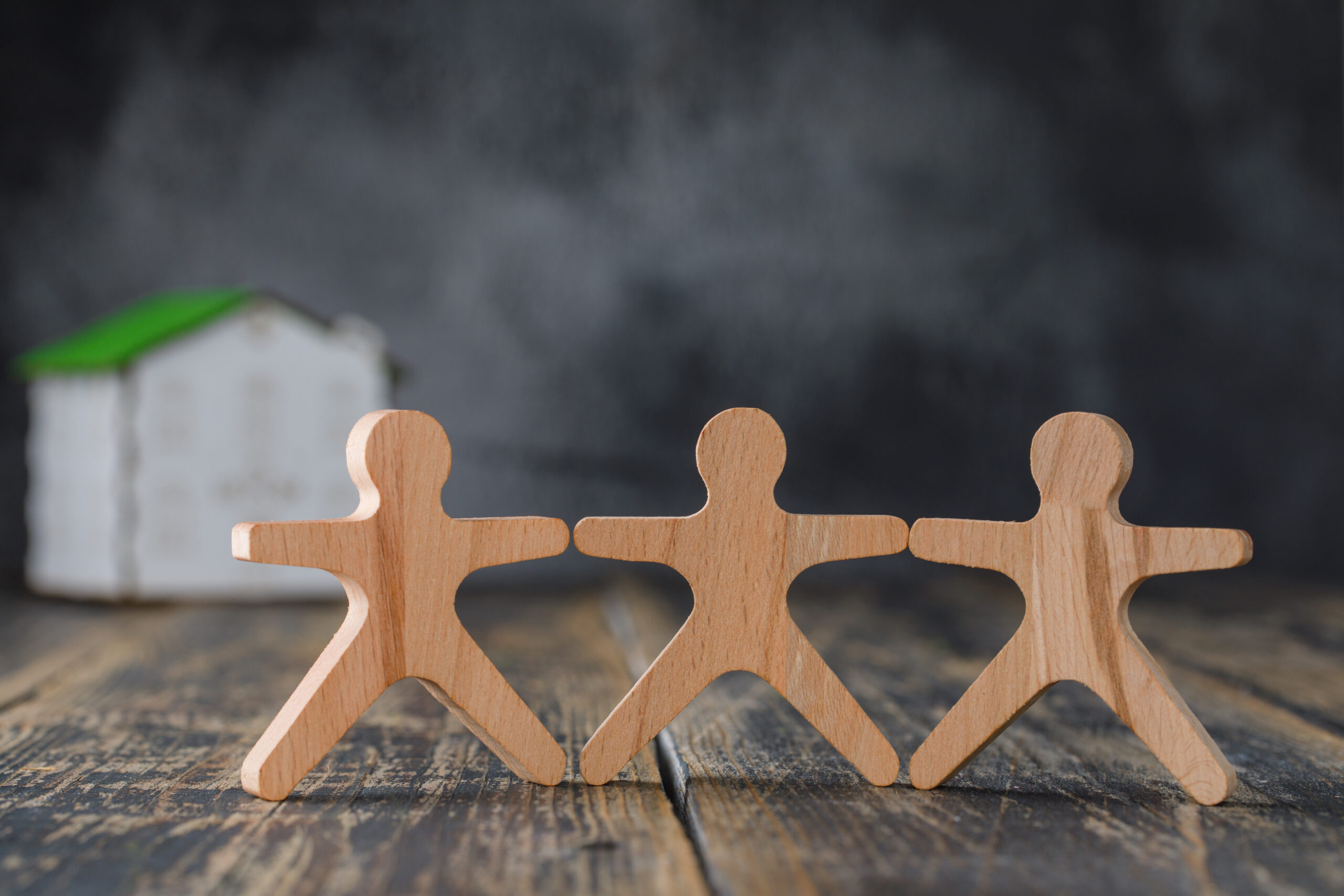 family safety concept with wooden figures of people, model house on wooden and foggy background side view.